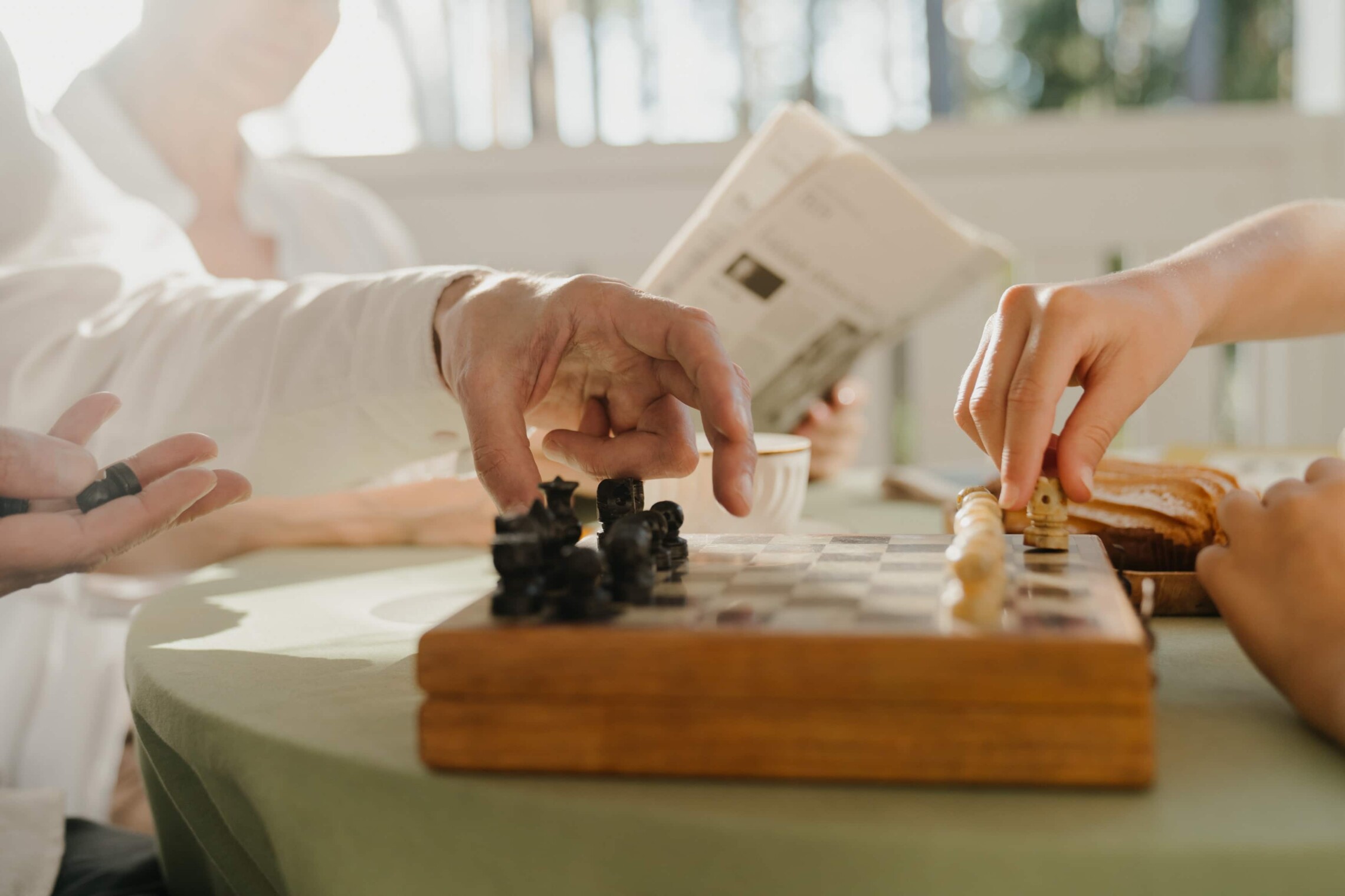 Two people playing chess and one person reading newspaper