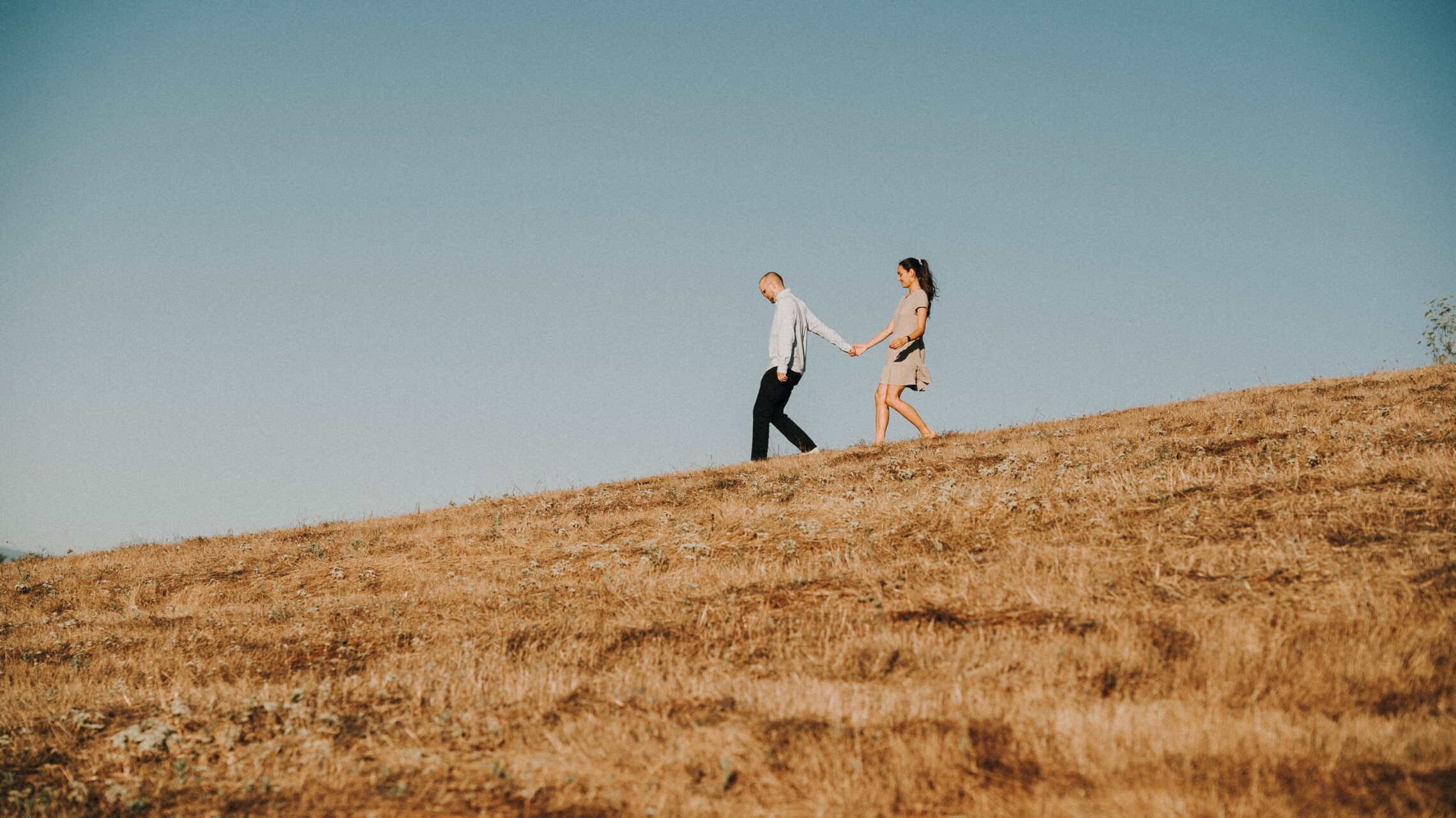 Two people walking down hill holding hands